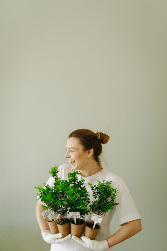 Cheerful woman holding pots of plants, promoting eco-friendly lifestyle indoors.